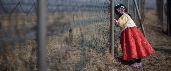 A girl wearing a traditional hanbok dress stands at a military fence facing towards North Korea at Imjingak park, South of DMZ, photo by Ed Jones